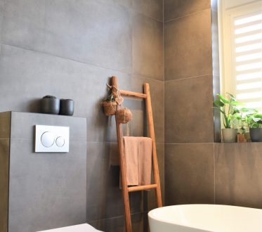 Badkamer in Noordwijk met donkergrijze betonlook tegels, een houten ladder en een vrijstaand bad