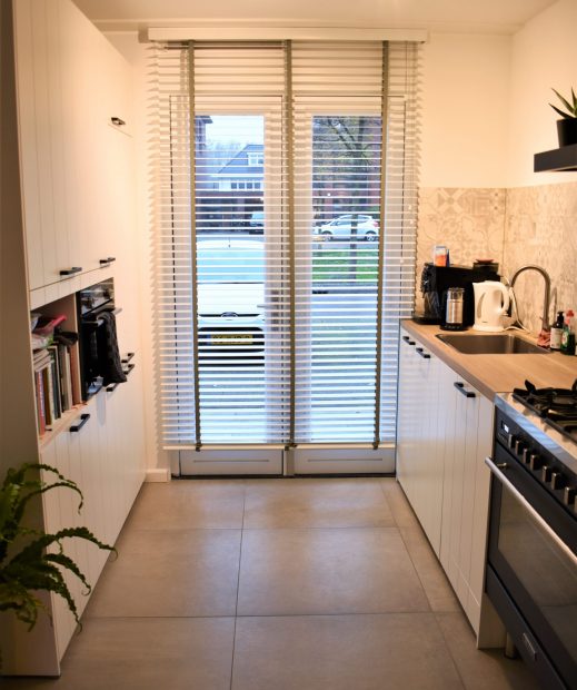 Keuken in Noordwijk met witte kasten en grote lichte betonlook vloertegels tot aan de tuindeuren