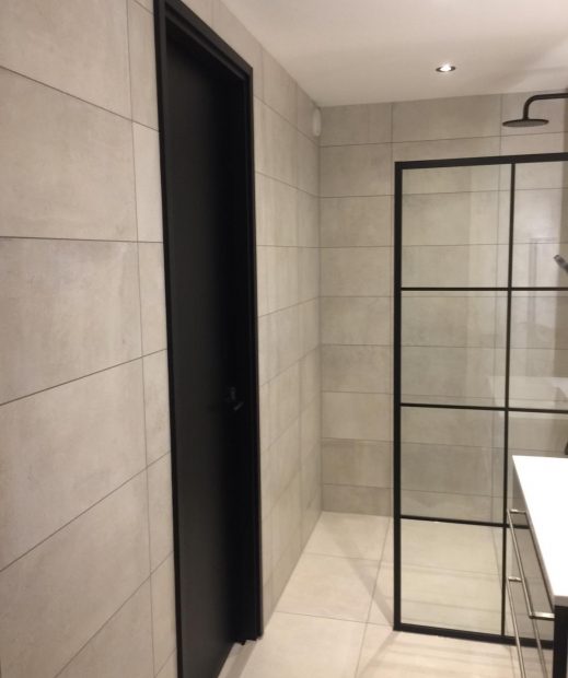 Badkamer in Valkenburg met lichte betonlook wandtegels en een douche met zwart profiel
