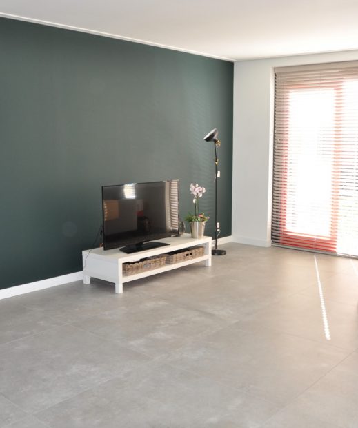 Woonkamer in Valkenburg met grote lichtgrijze betonlook vloertegels en een groene accentwand
