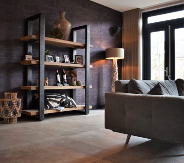 Woonkamer in Noordwijk met grote lichte betonlook vloertegels, een grijze bank en een open boekenkast