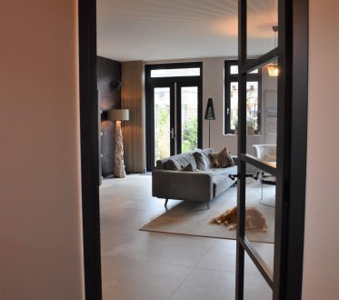 Woonkamer in Noordwijk met grote lichte betonlook vloertegels en een stalen binnendeur