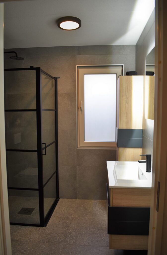 Badkamer in Noordwijk met terrazzo look vloertegels, donkere betonlook wandtegels en een houten kast