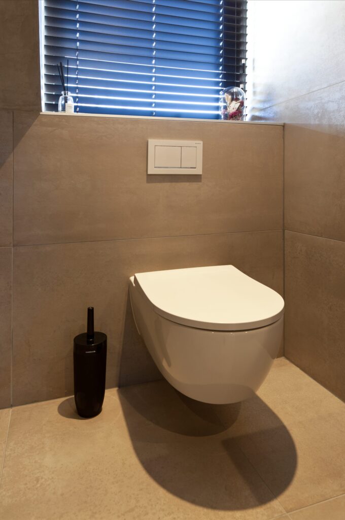 Toilet in Rijnsburg met grote metallook wandtegels, een lichte vloer en een hangend toilet