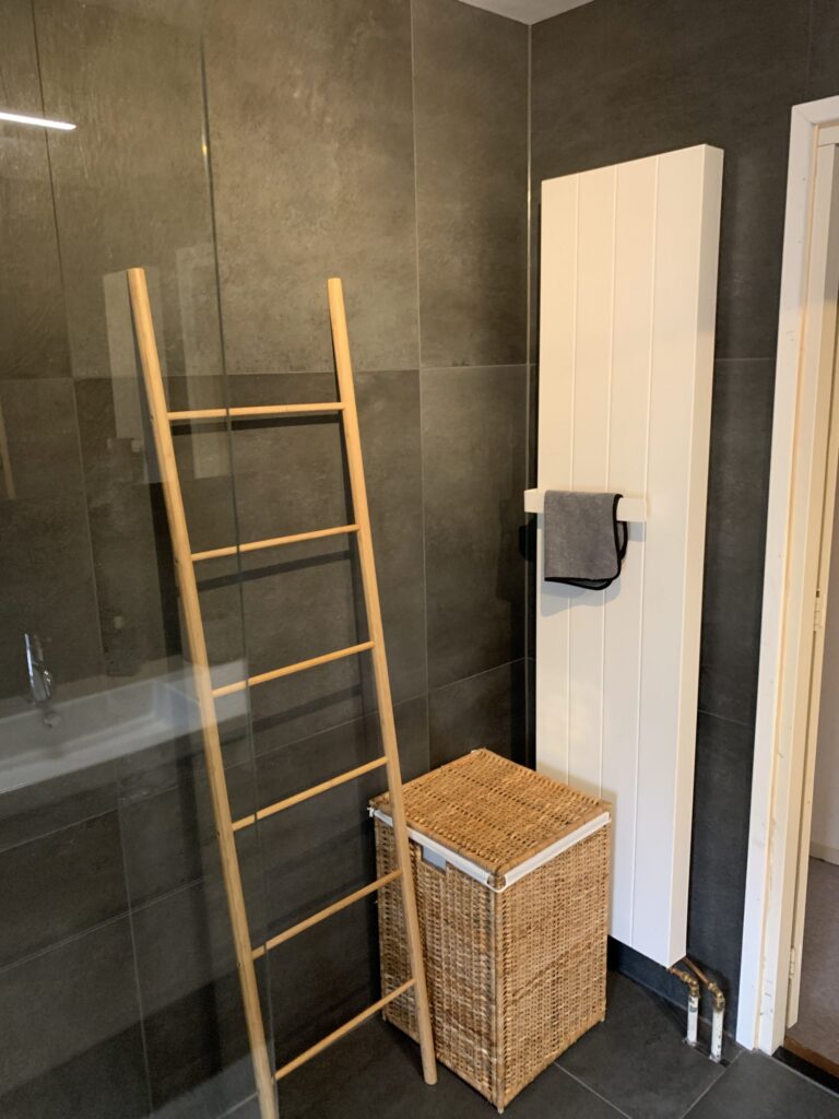 Badkamer in Katwijk met donkere matte tegels, inloopdouche en een houten handdoekladder