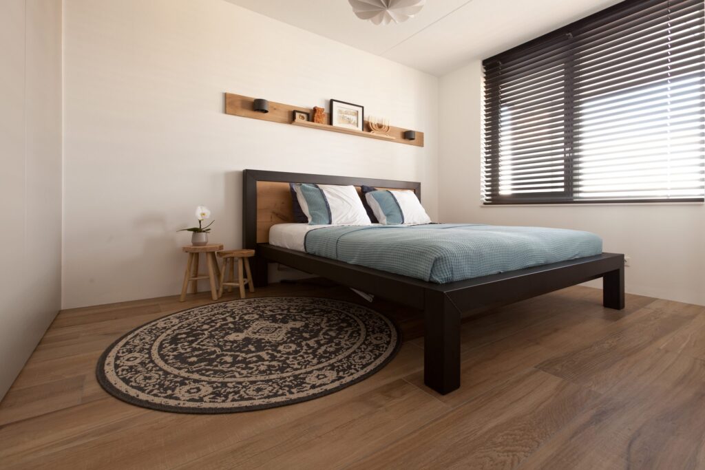 Slaapkamer in een appartement in Noordwijk met warme houtlook vloertegels, een houten bed en een rond kleed