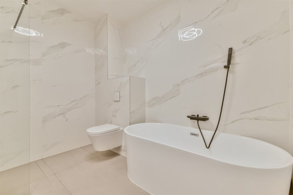 Badkamer in Amsterdam met glanzende witte marmerlook tegels en een vrijstaand bad