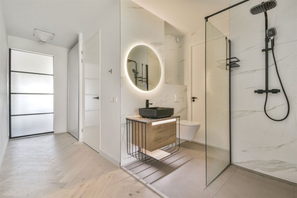 Badkamer in Amsterdam met witte marmerlook tegels, een ronde spiegel en een inloopdouche