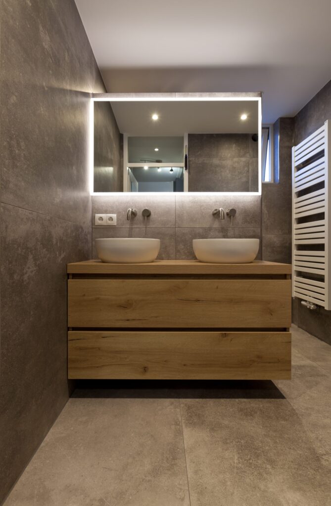 Badkamer in Katwijk met betonlook tegels van 100×100, een zwevend eiken badmeubel en een verlichte spiegel