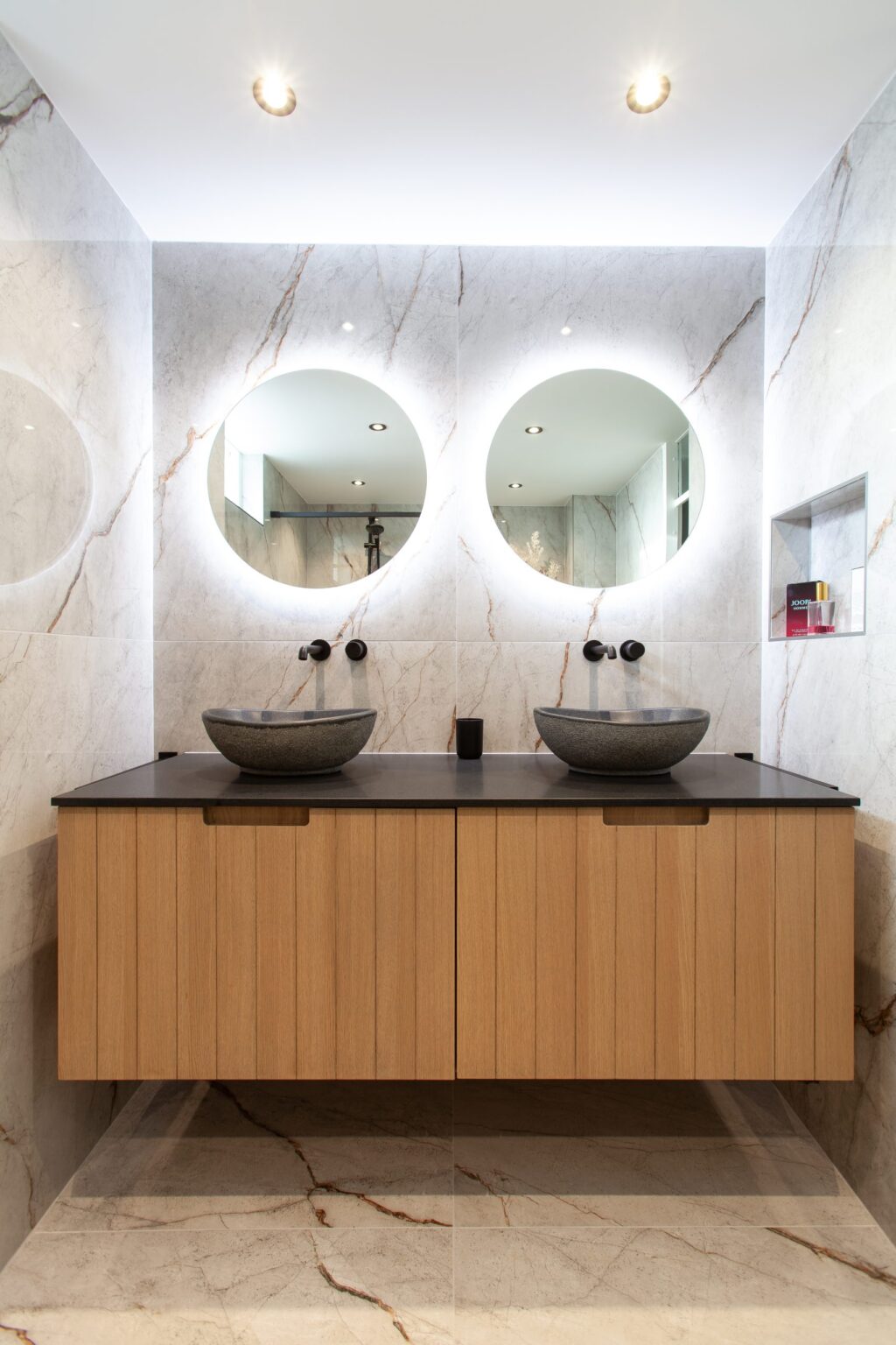 Badkamer in Leiderdorp met marmerlook tegels, een zwevend houten badmeubel en twee ronde spiegels