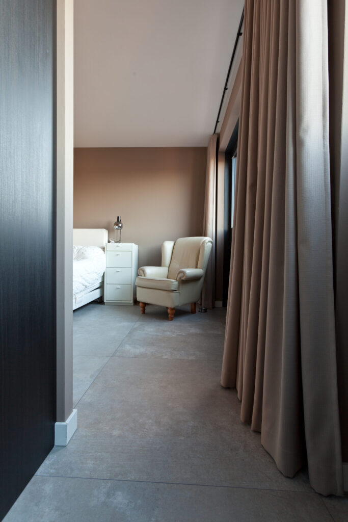 Kamer in Noordwijk met grote betonlook vloertegels, een donkere wand en een fauteuil