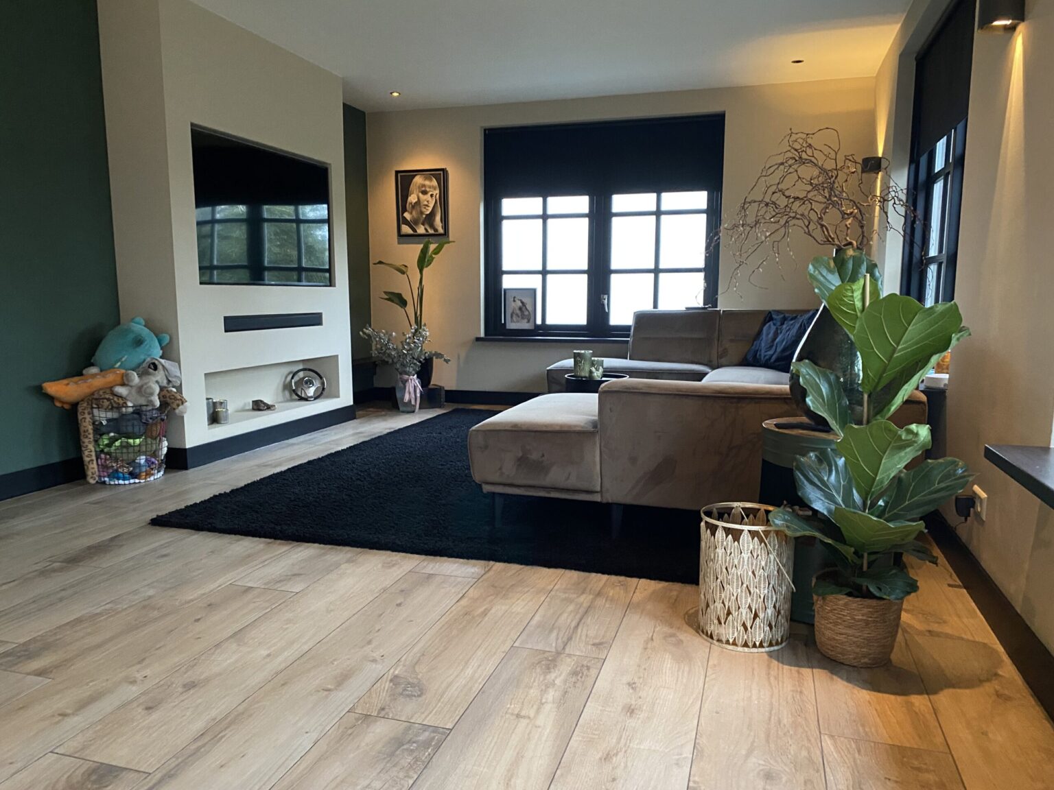 Woonkamer in Noordwijk met lichte houtlook vloertegels, een grote plant en een zwart vloerkleed