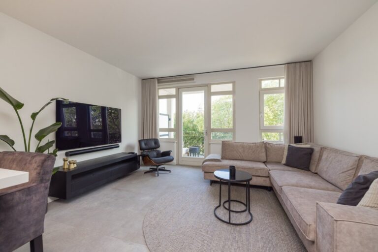 Woonkamer van een appartement in Leiden met lichtgrijze betonlook tegels van 100×100 en een balkondeur