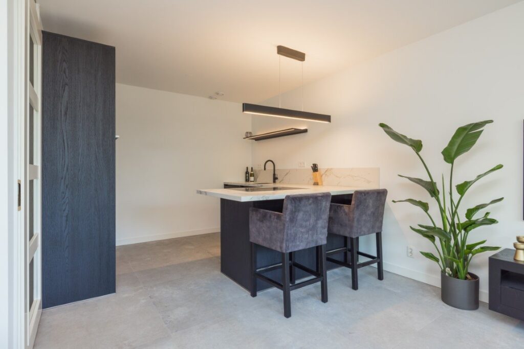 Keuken met bar en donkere kasten op lichtgrijze betonlook vloertegels van 100×100 in een appartement in Leiden