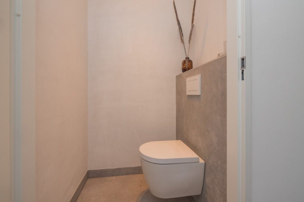 Toilet in Leiden met betonlook tegels op de vloer en tegen de voorzetwand van het hangend toilet