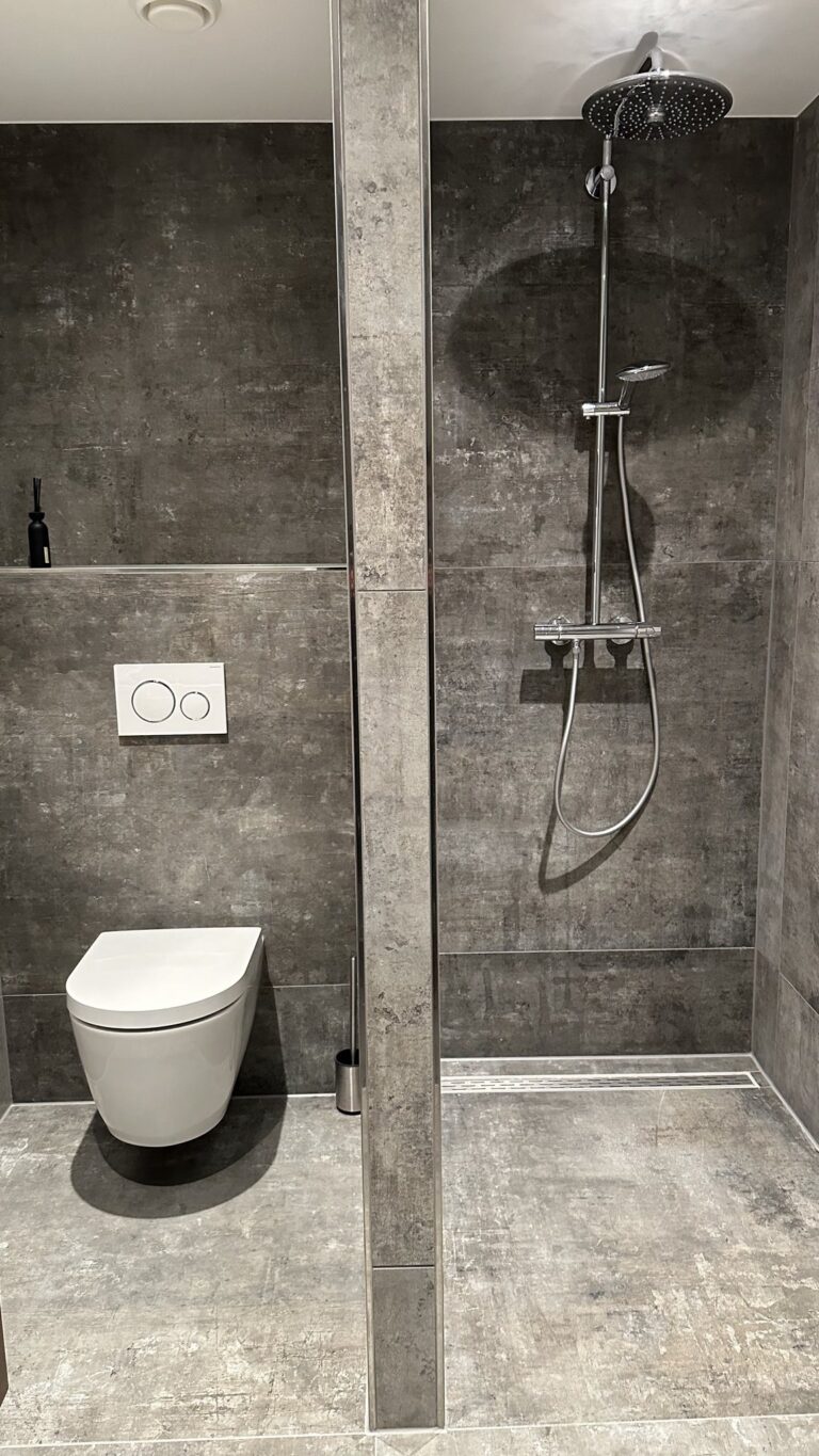 Badkamer in Noordwijkerhout met grijze betonlook tegels van 100×100 op vloer en wand, een hangend toilet en een inloopdouche