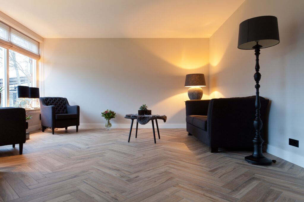 Woonkamer in Oegstgeest met houtlook tegels van 15×60 in visgraat, zwarte fauteuils en een bank
