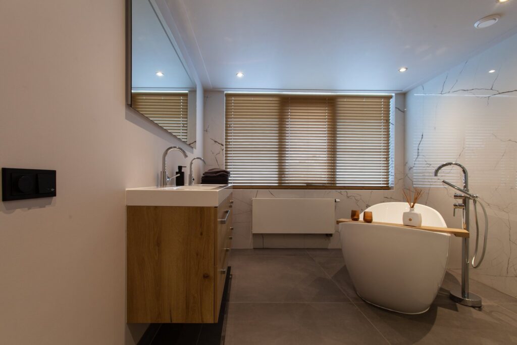Badkamer in Warmond met antraciet betonlook vloertegels van 120×120, witte glanzende marmerlook wandtegels van 120×120 en een vrijstaand bad