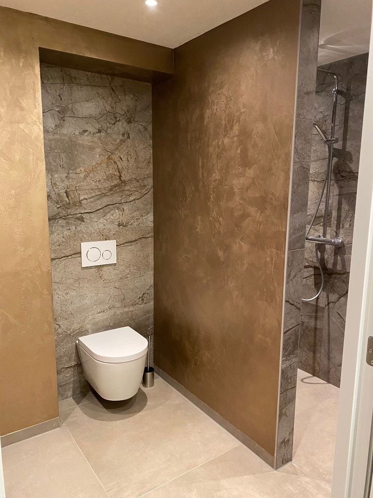 Badkamer in Voorhout met marmerlook tegels van 60×120 achter het toilet en in de douche, en een lichte betonlook vloer van 90×90