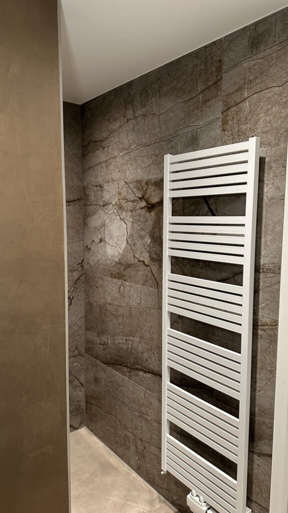 Douchewand met grote marmerlook tegels van 60×120 en een witte handdoekradiator in Voorhout