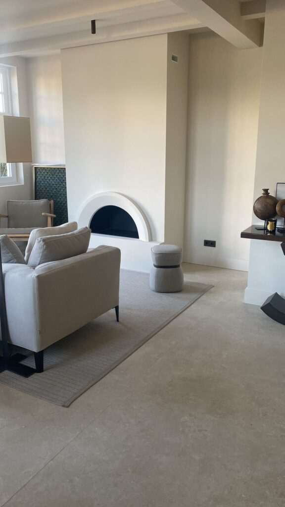 Woonkamer in Wassenaar met een witte haard met boog en een vloer van beige natuursteenlook tegels van 120×120