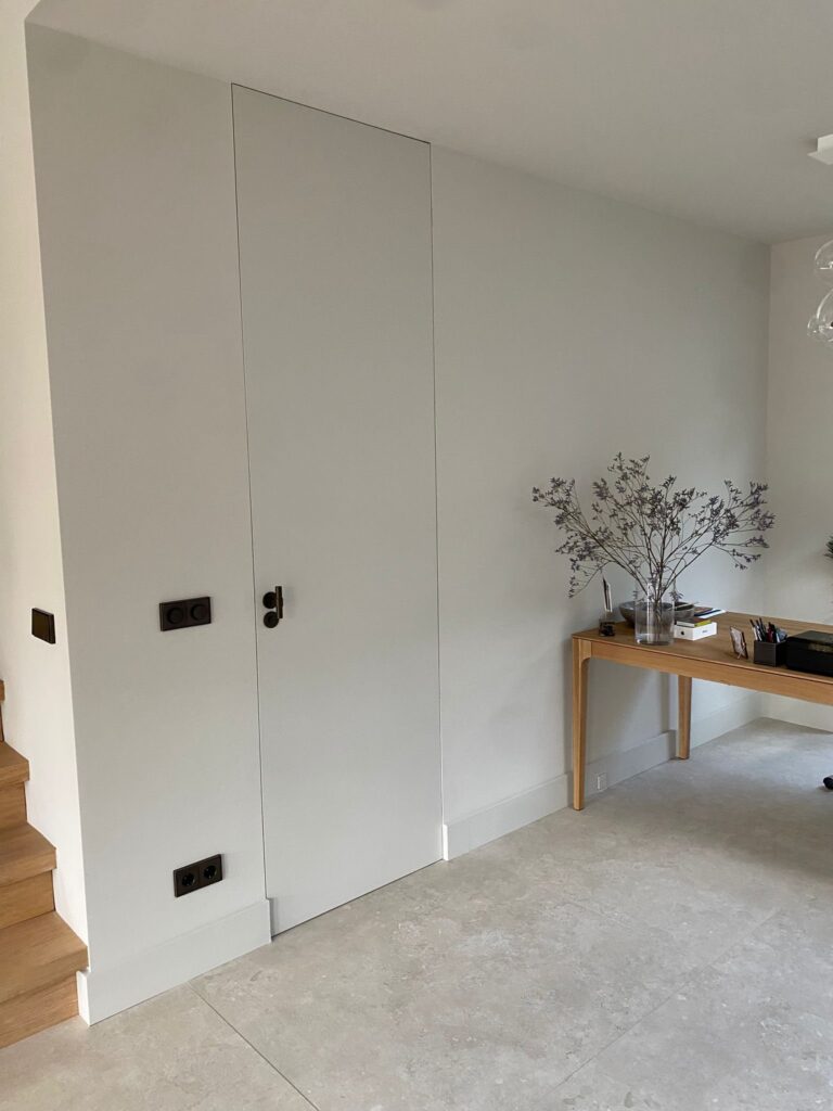 Strakke wand met verdekte deur en een houten bureau op beige natuursteenlook tegels van 120×120 in Wassenaar