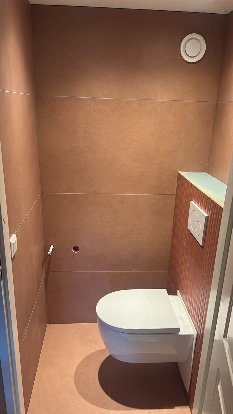 Toilet in Leiden met terracottakleurige tegels van 60×120 op vloer en wanden en bordeauxrode decortegels van 5×40 op het inbouwreservoir